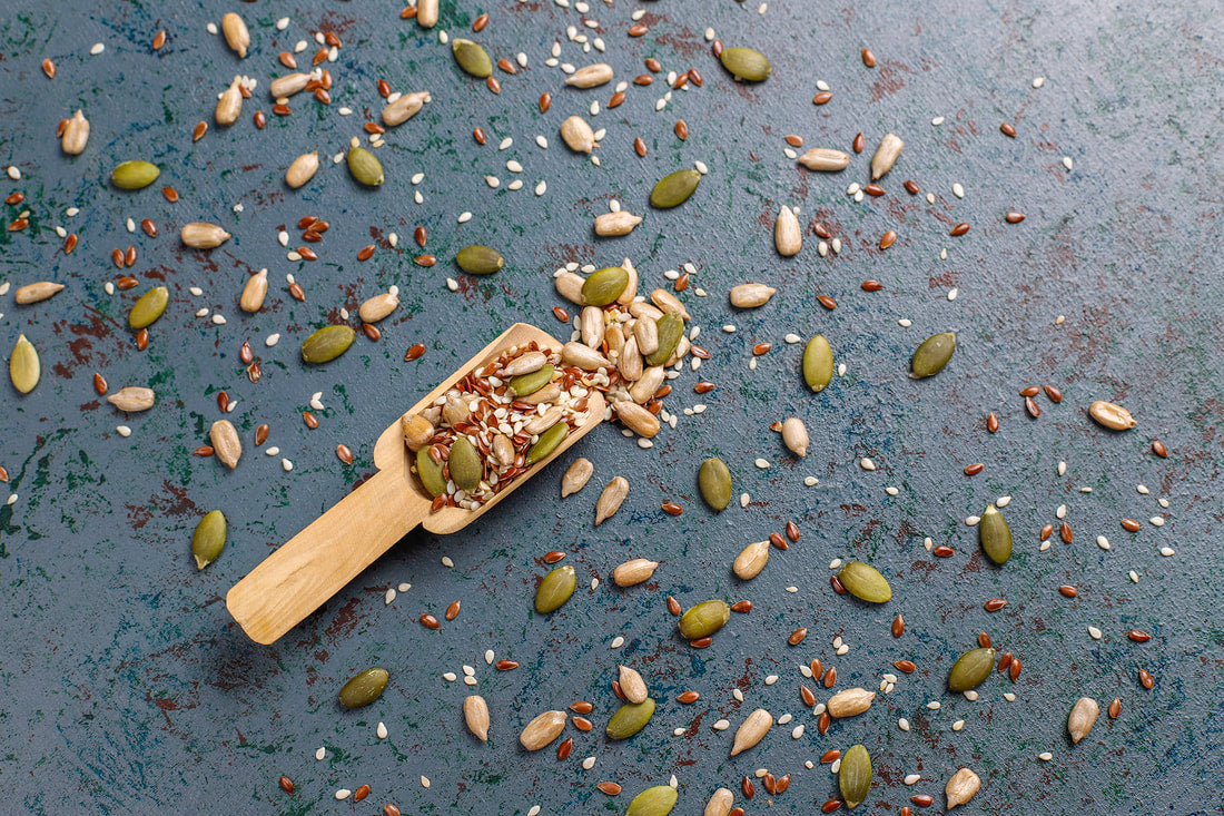 Assorted seeds and grains including pumpkin, sunflower, and sesame scattered on a dark surface.