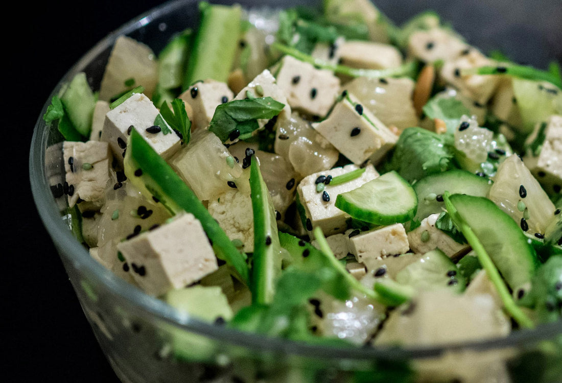 Fresh tofu and cucumber salad with black sesame seeds in a glass bowl.