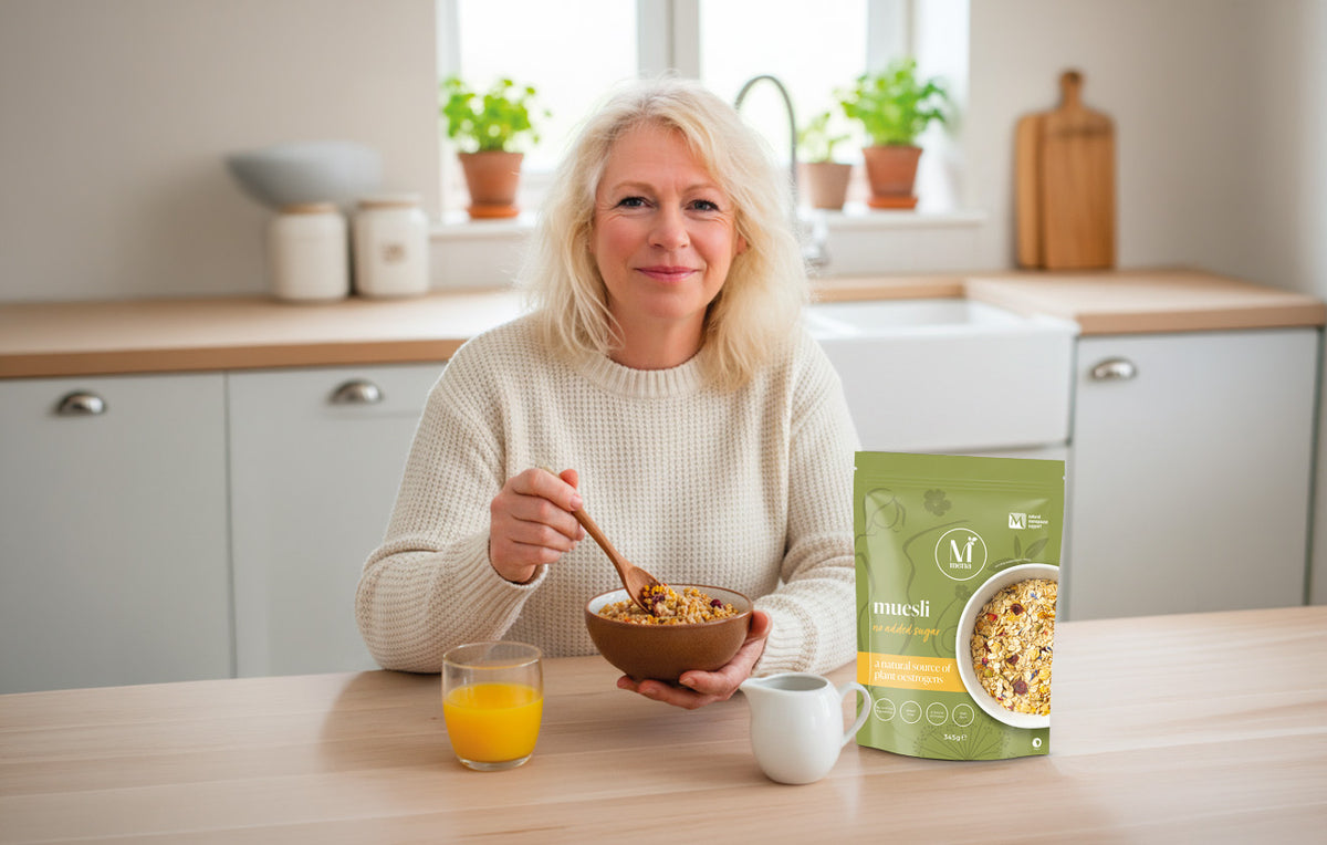 Smiling blonde woman eating plant-based muesli with orange juice in a bright kitchen.