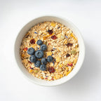 A white bowl filled with Mena Pause muesli topped with fresh blueberries and dried fruit.