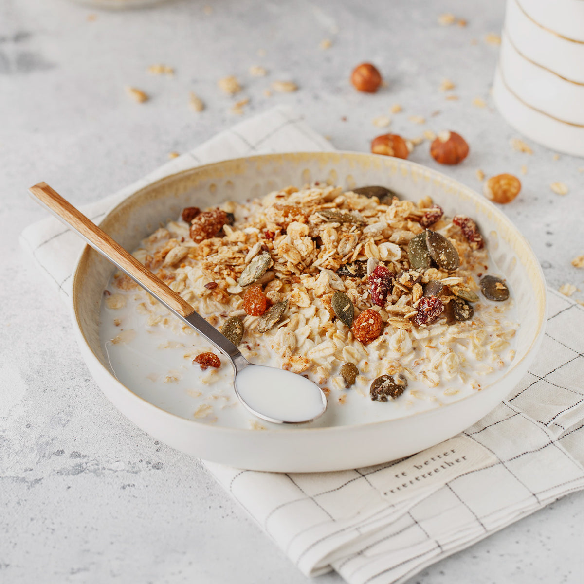 Mena Pause muesli with oats, seeds, and dried fruit in a bowl with milk and a spoon
