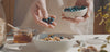 video showing blueberries being added to a bowl of granola, a breakfast bowl, honey dripping from a honey spoon